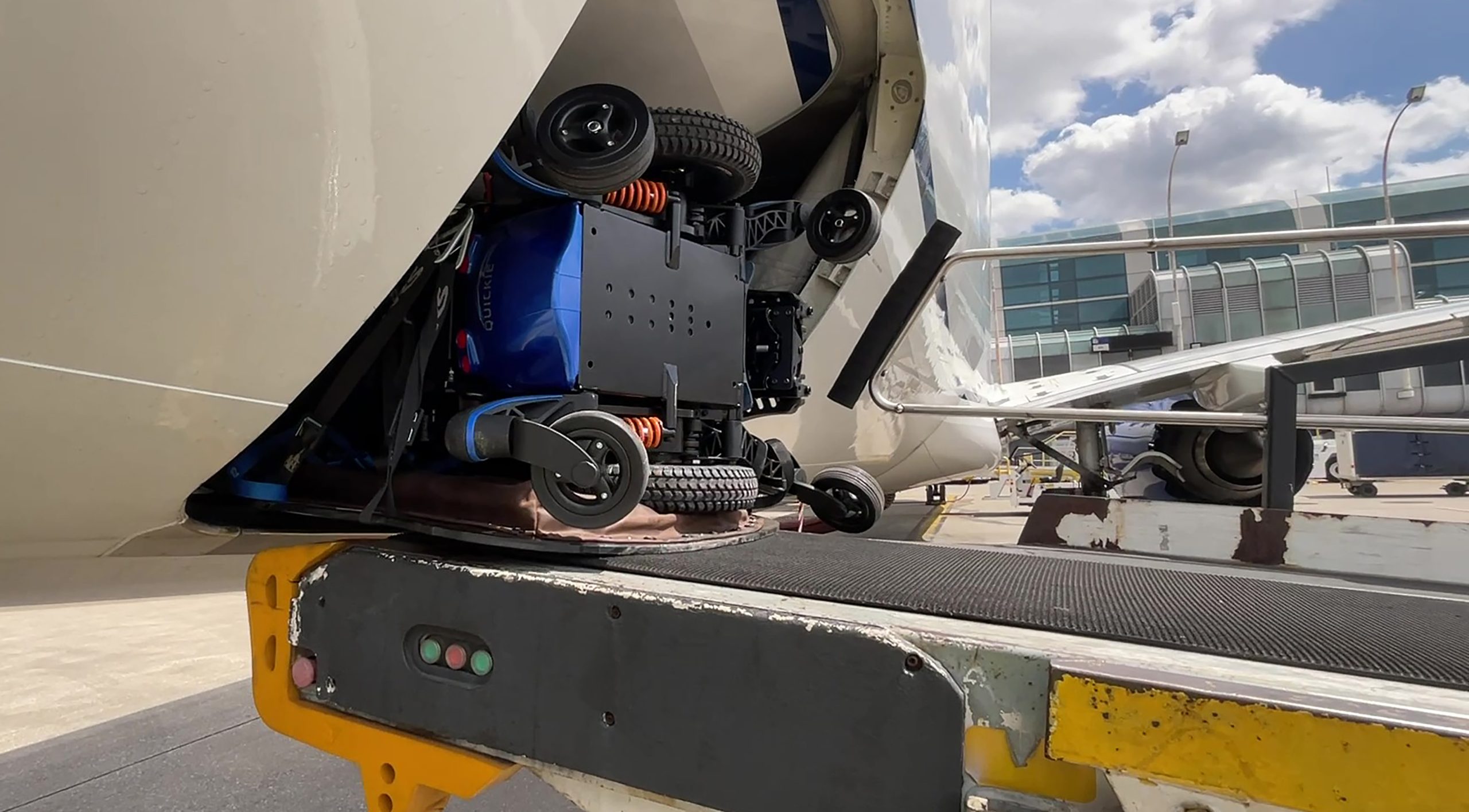 Tipped powered wheelchair and padded tipping plate package entering doorway of cargo hold from belt loader.